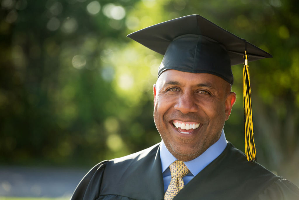 WE – High School Equivalency (1) An African American adult man in his mid 40's in a cap and gown celebrating his high school equivalency diploma program