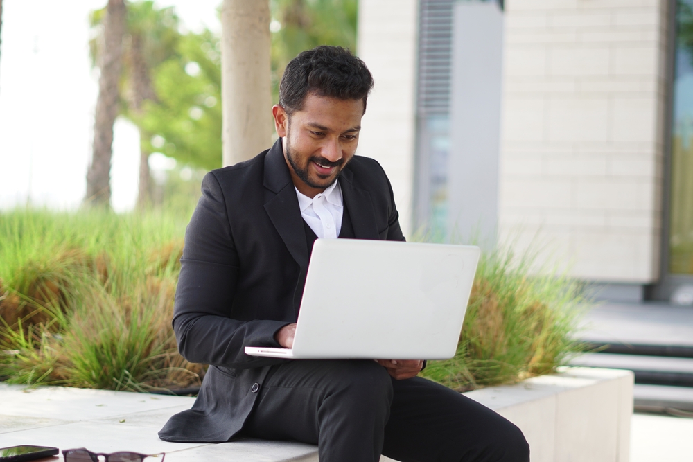 Man typing on laptop, outside, smiling.