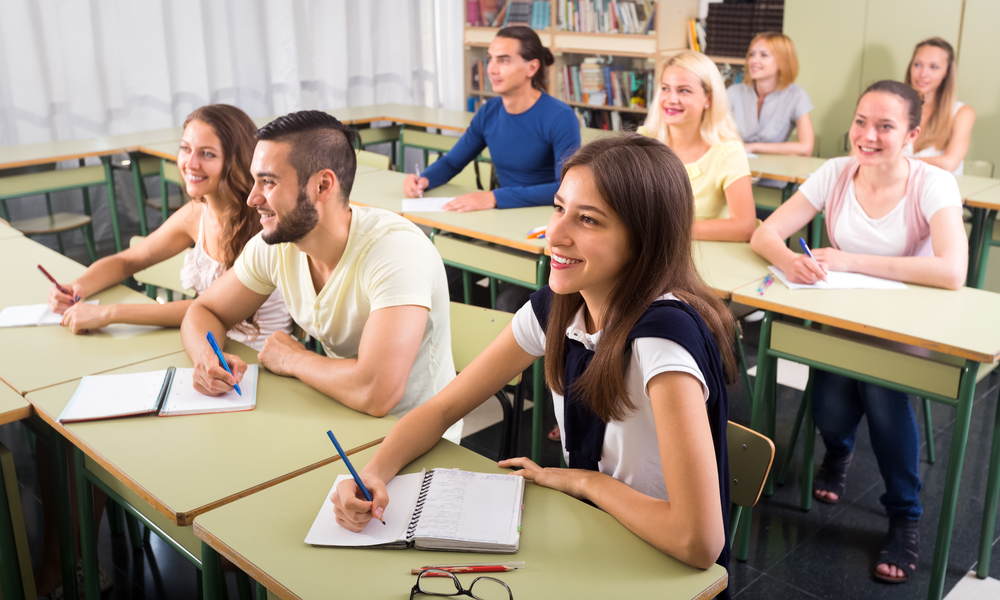 Group of students at desk taking notes and smiling.