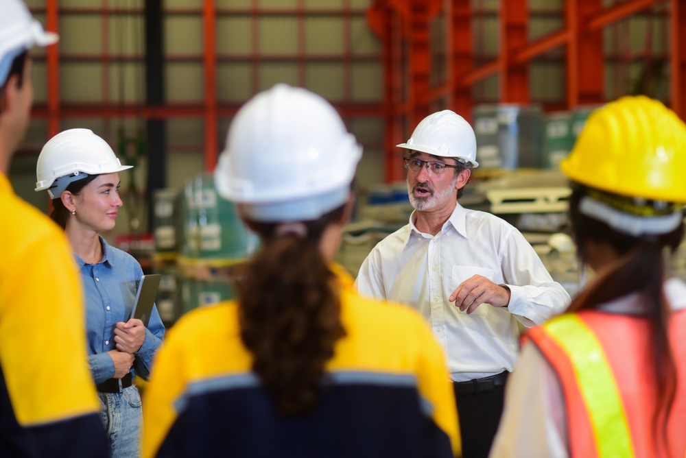 A man guides a safety meeting with a team of workers